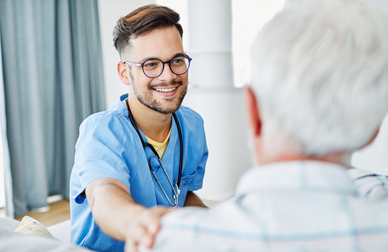 Ein lächelnder männlicher Krankenpfleger schüttelt die Hand eines älteren Mannes in einem freundlichen Moment.