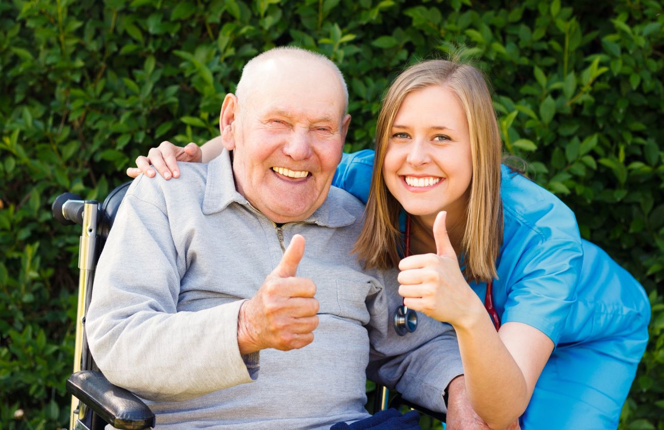 Eine Pflegerin und ein älterer Mann zeigen Daumen hoch und strahlen Freude und Zufriedenheit aus.