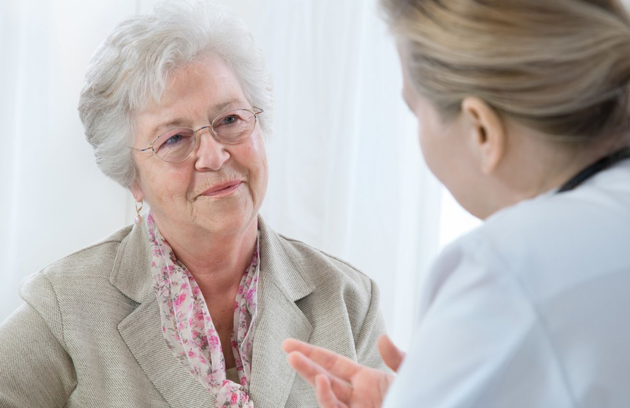 Eine Frau im Gespräch mit einer älteren Frau, die aufmerksam zuhört und eine freundliche Mimik zeigt.