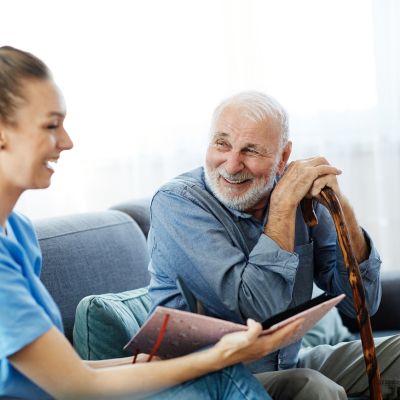 Eine fröhliche Frau und ein älterer Mann sitzen auf einer Couch und teilen einen herzlichen Augenblick miteinander.