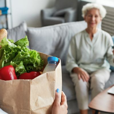 Eine Frau hält eine Papiertüte mit Gemüse und eine Wasserflasche in der Hand.